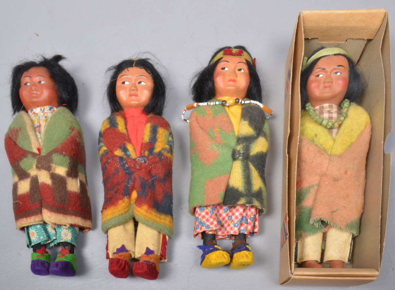 (4) Skookum Dolls: (4) Skookum dolls to include #4029 young boy, 9", plastic feet, no label, green painted wooden bead necklace and green cloth headband, in box, squaw baby, 9" felt feet, no label, purple orange and mag