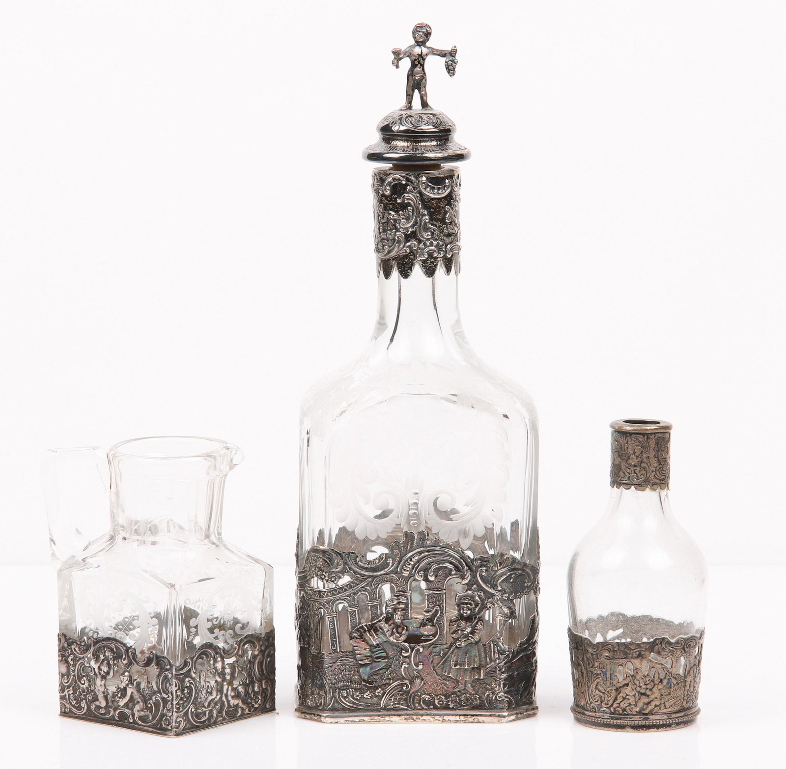(3) German Glass Decanter, Pitcher, Bottle: (3) German glass decanter, pitcher, bottle to include Storck and Sinsheimer Hanau etched glass decanter in pierced figural silver frame depicting courting scenes, with matched silver repousse collar, 