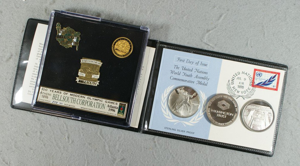 Assorted medals and pins consisting of (2) 1 troy: Assorted medals and pins consisting of (2) 1 troy oz. Wilmington trust .999 silver rounds, a 1 troy oz./ sterling medal on cover and (3) commercial 1996 Olympics metal pins in a plastic case.