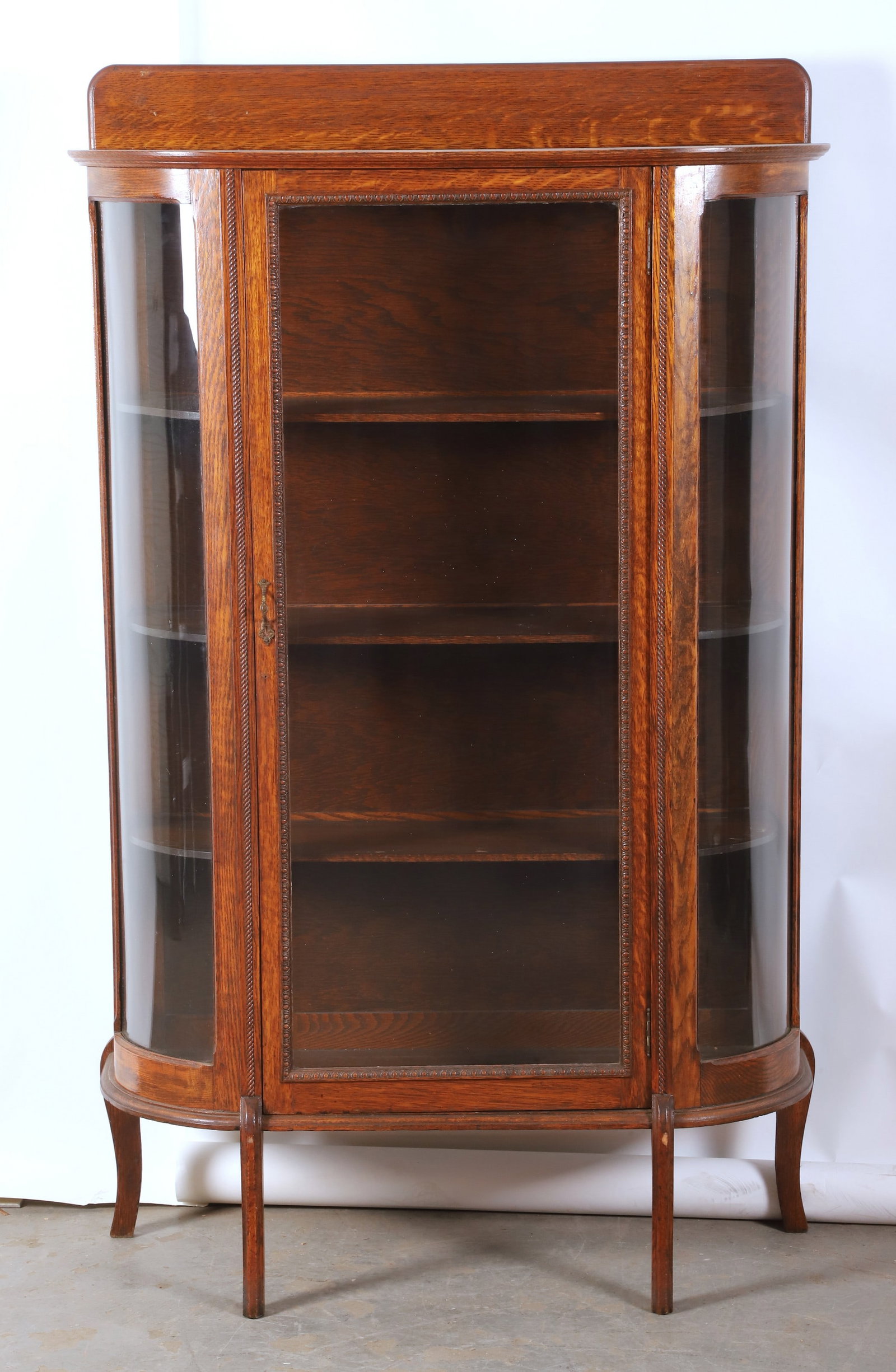 Oak glass door curio: Oak glass door curio, backslash at top, single glass door, flanked by 2 curved side glass windows, on figured sabre legs, 3 wood shelves, 66"H x 39"W x 16"D