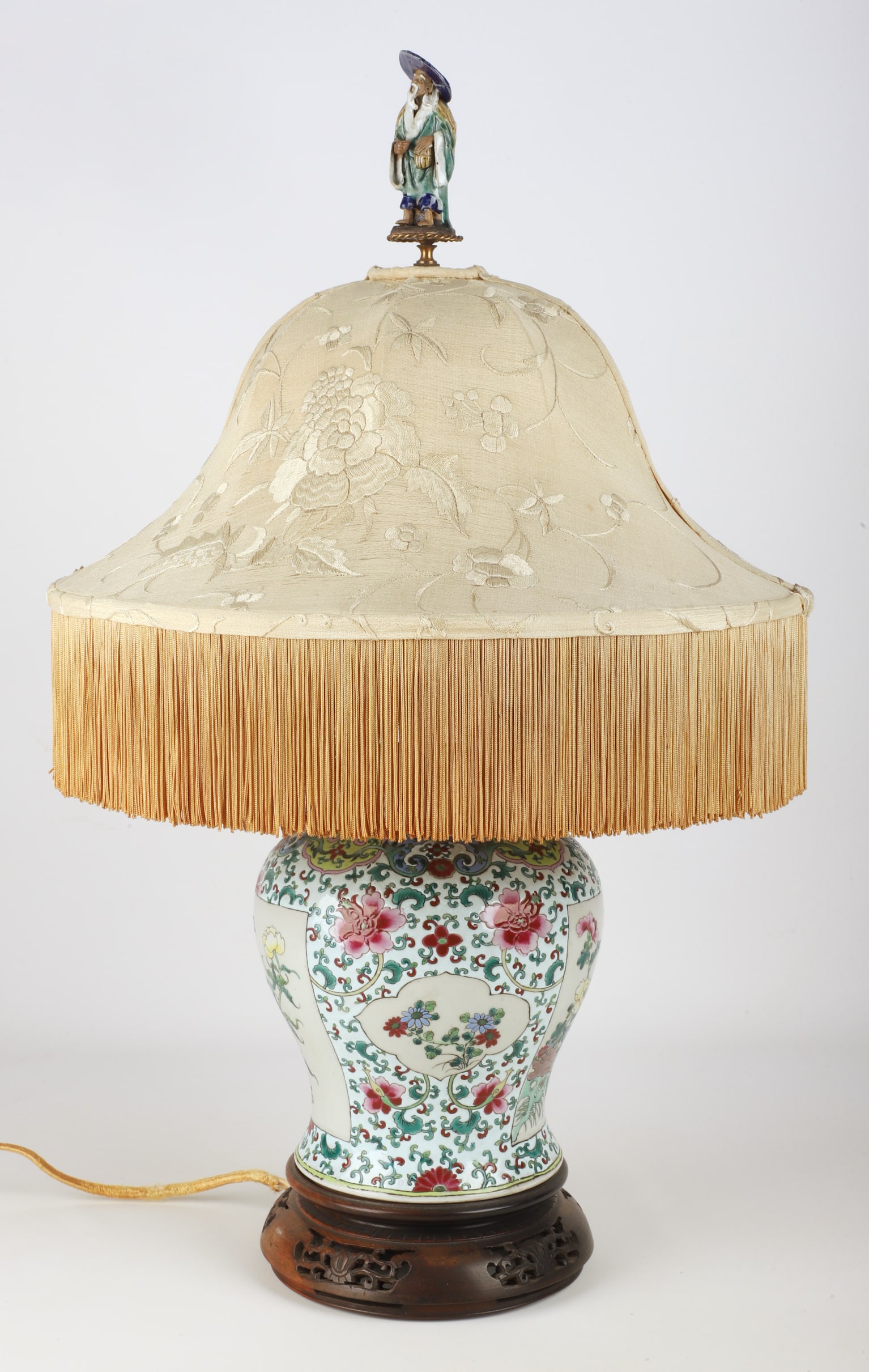 Chinese Famille Rose Jar as Lamp: Chinese famille rose jar as lamp, raised on pierced wood base with embroidered floral silk fringed shade, a figural pottery finial, 28"H