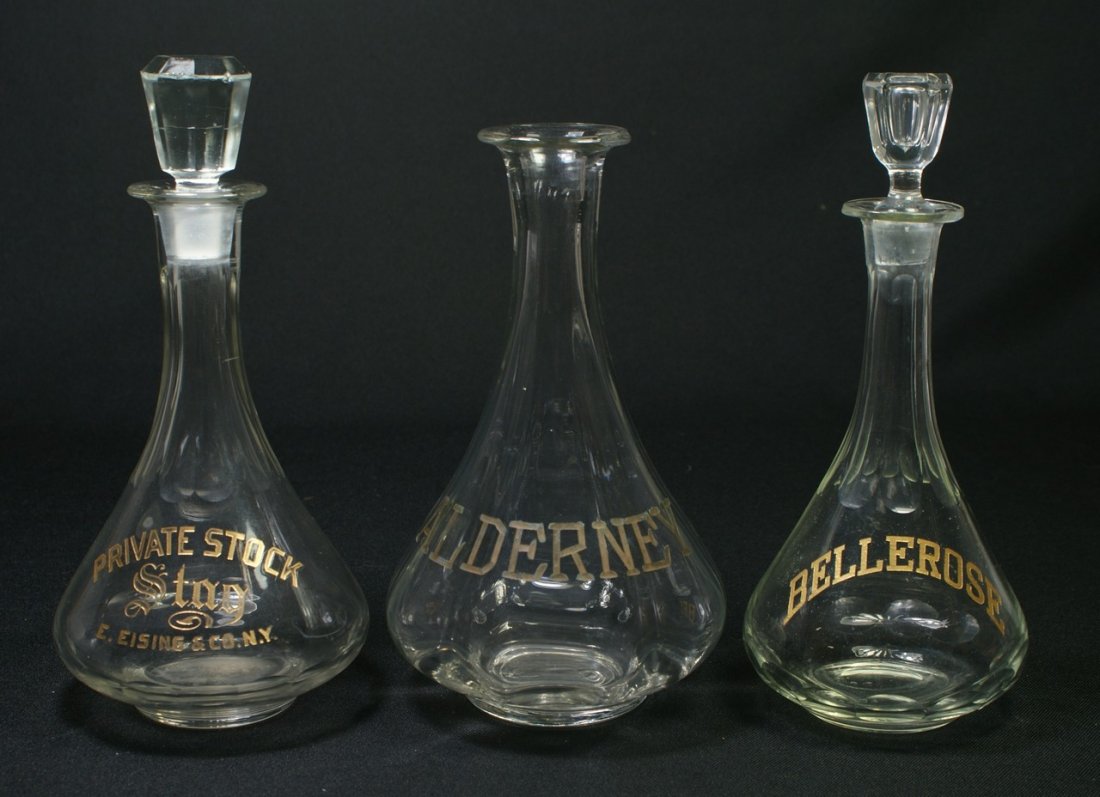3 clear glass back bar bottles with gilt & etched: 3 clear glass back bar bottles with gilt & etched decoration, ALDERNEY, BELLEROSE, PRIVATE STOCK, STAG, E. EISING & CO, NY, tallest 10", one missing stopper, both stoppers with roughage around bottom,