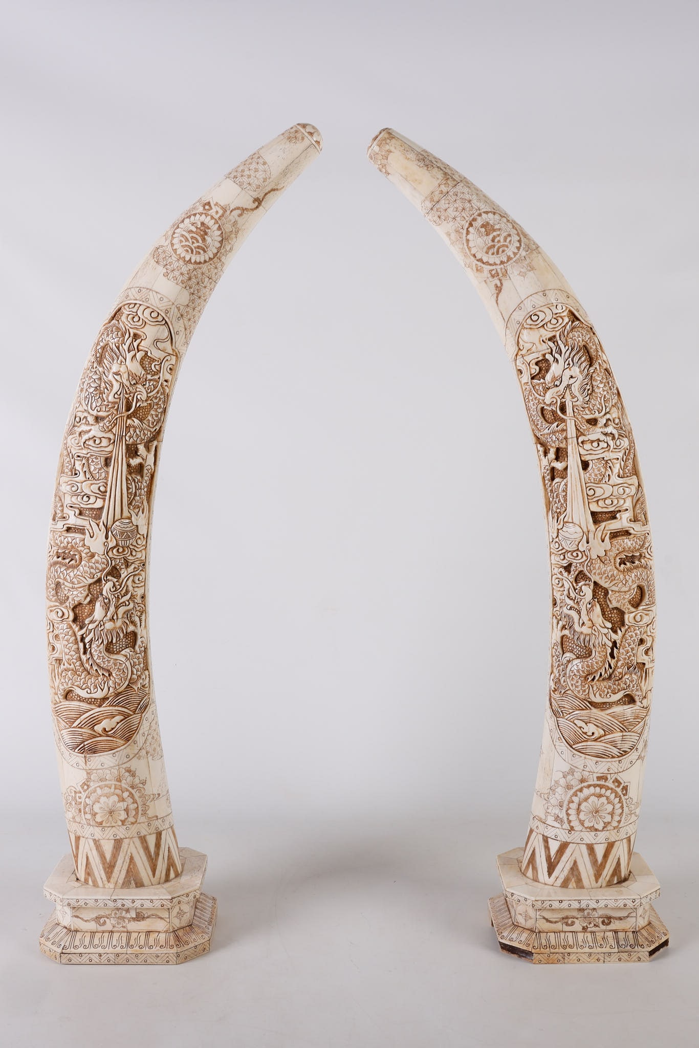 Chinese Carved and Inked Bone Veneered 'Tusk' Pair: Chinese Carved and Inked Bone Veneered Tusk Pair, relief carved scene depicting dragons, a flaming pearl, wind bars, waves and assorted floral and geometric motifs, raised on stepped bone veneered bas