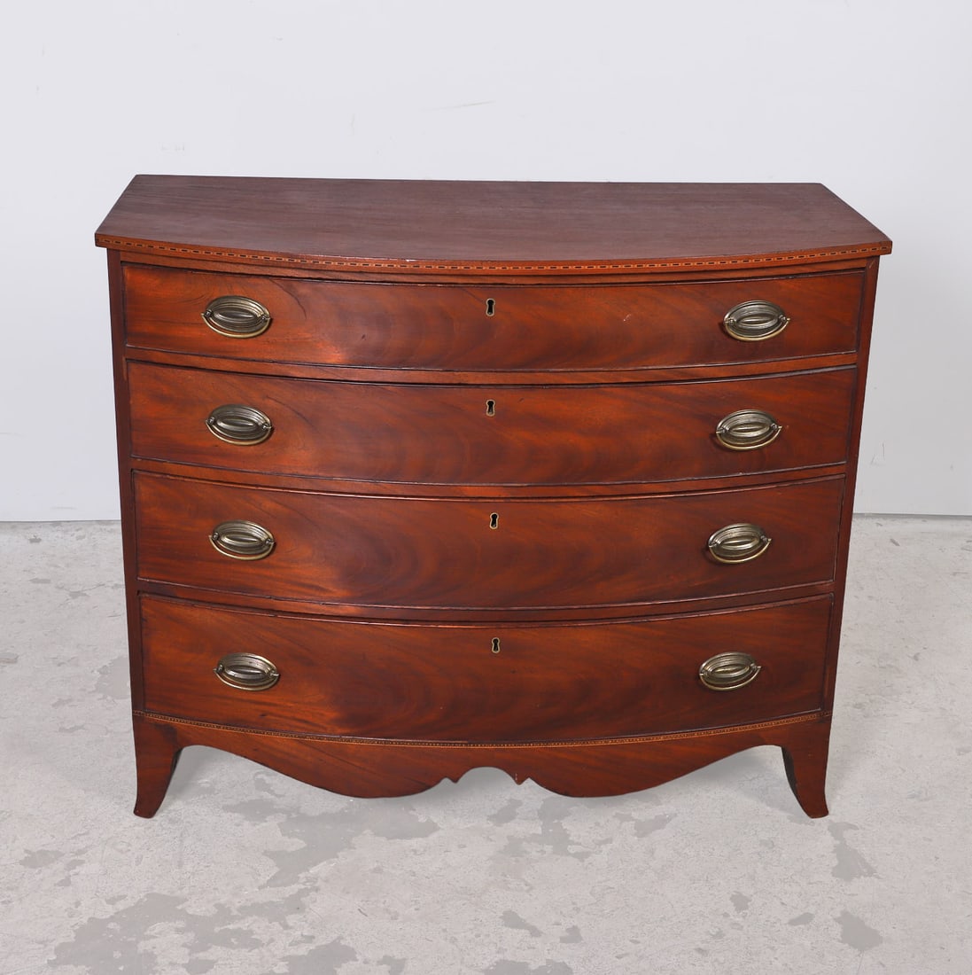 Hepplewhite Style Mahogany Bachelor's Chest: Hepplewhite style mahogany bachelor's chest, small checkerboard inlay on top rim, four graduated drawers, bronze escutcheons, w/drop bails, scalloped apron, stylized bracket foot, 37"H x 44 1/2"W x