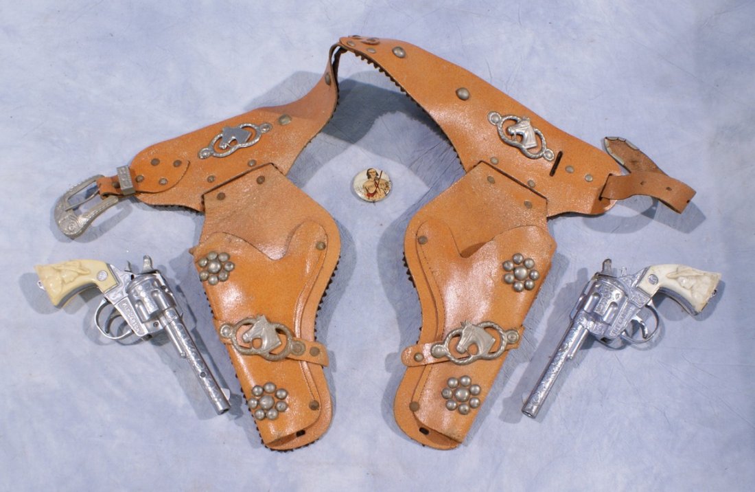 Leather double holster with metal horse head decoration: Leather double holster with metal horse head decoration with (2) Kilgore Kit Carson cap guns, guns 8" long, with a pin back button