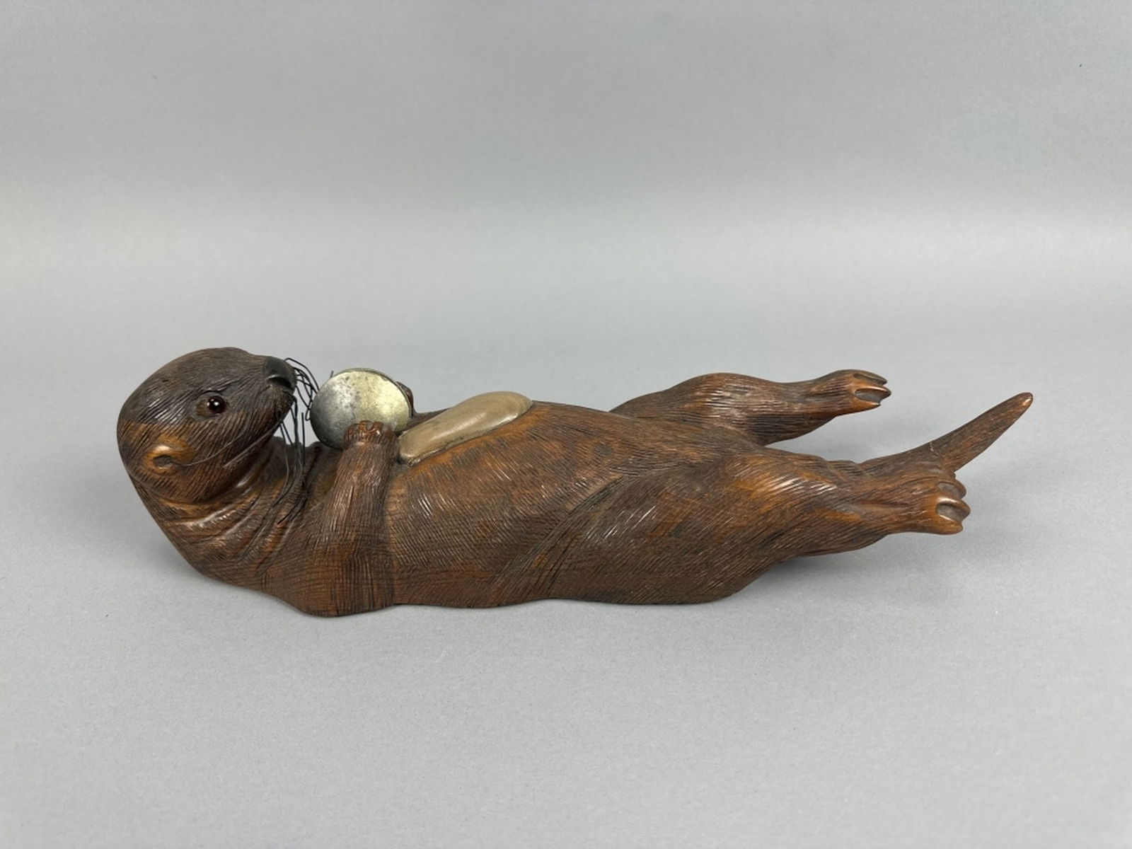 Tom Taber Hand Carved Otter: Montana, glass eyes, natural sided, nice form laying on its back holding a shell, crack through tail that has been reset, otherwise in good condition, Ralph Kandt Collection, 15.5"L, est. 100 - 200