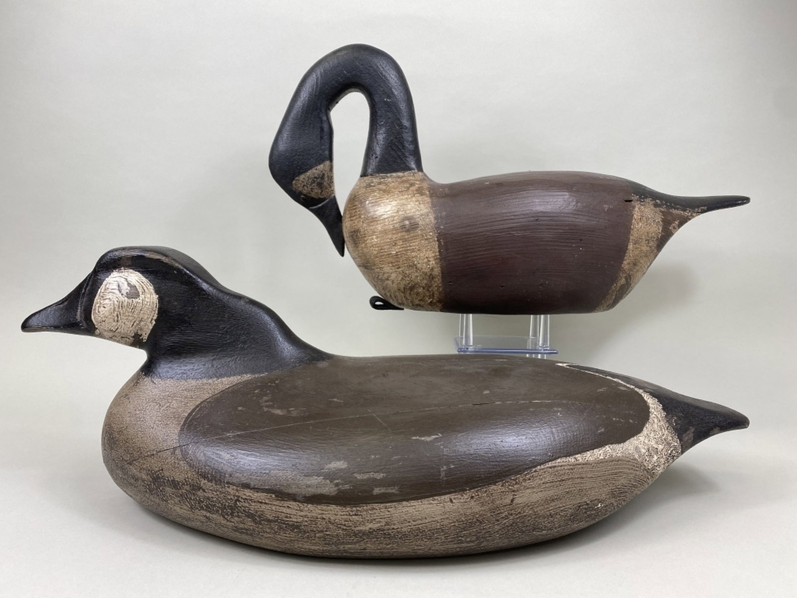2 Canada Geese Decoys: by unknown carvers, 1 has tack eyes, hollow body, original paint, in preening position, small dings, dents, "SA" carved in bottom & 1 has no eyes, solid body, old repaint, paint loss on sides & bottom