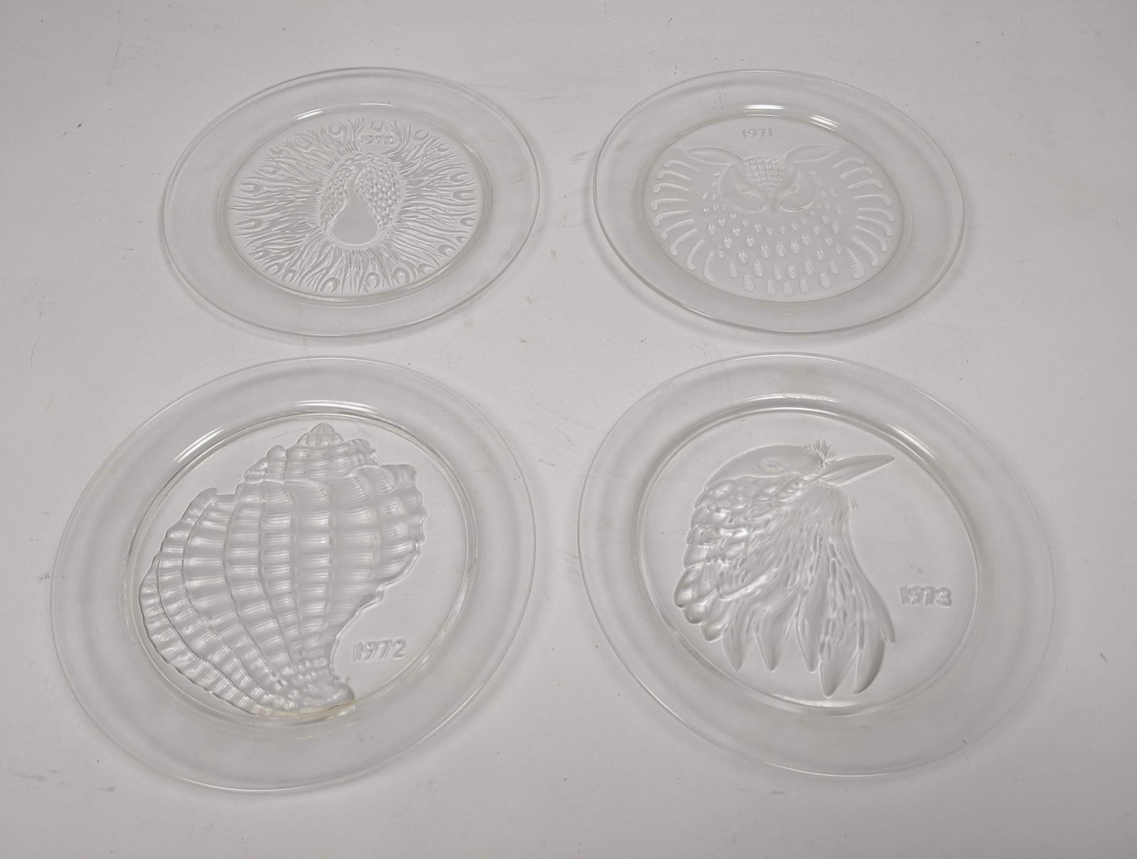 LALIQUE France Annual Plates. 1970, '71, '72, '73. Feat: LALIQUE France Annual Plates. 1970, '71, '72, '73. Featuring birds on three and one seashell place. -- Dimensions: : W: 8.25 inches: D: 8.25 inches ---