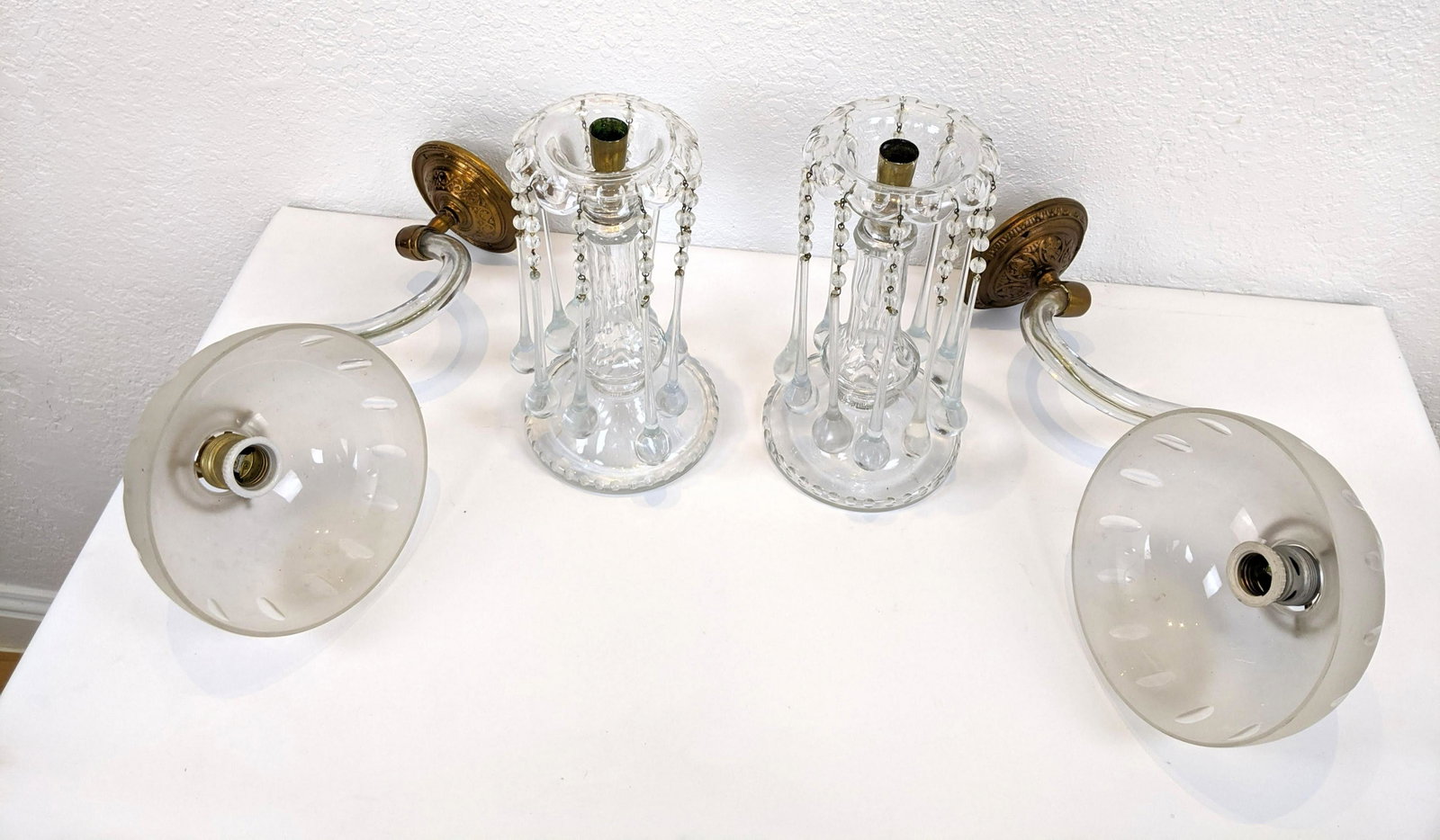 4pc Glass Lighting Lot. Pr glass S form wall sconces. F: 4pc Glass Lighting Lot. Pr glass S form wall sconces. Frosted glass shades & brass mounts. Very good condition. Pr of clear crystal prism candle sticks with long tear drop prisms and floral bobeche. E