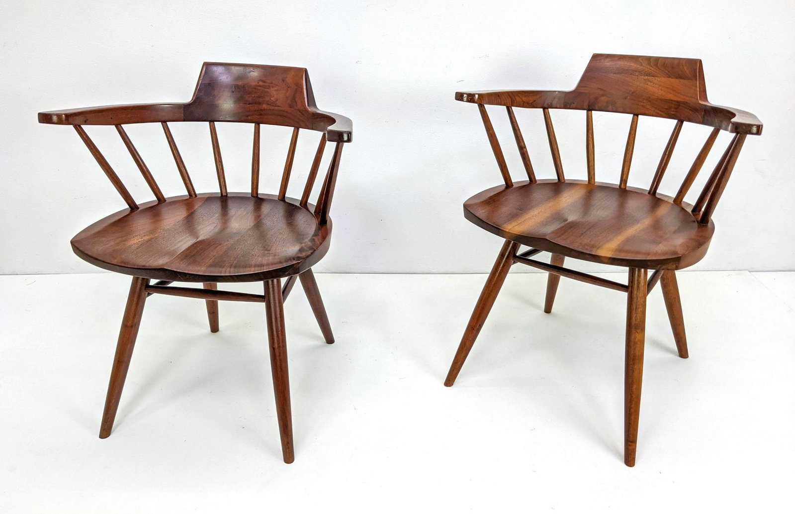 Pr GEORGE NAKASHIMA Walnut Captain's Chairs. American: Pr GEORGE NAKASHIMA Walnut Captain's Chairs. American Black Walnut. Bowed backrests with spindle construction. Note: This item and all the George Nakashima items from lot 695 though 742 were acquired 