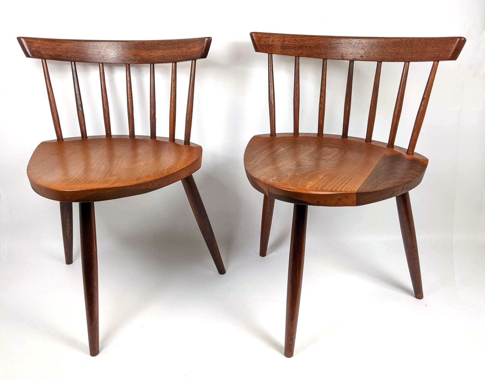 Pr GEORGE NAKASHIMA American Walnut Mira Chairs. Bowed: Pr GEORGE NAKASHIMA American Walnut Mira Chairs. Bowed backrests with spindle construction. Three legged base. Note: This item and all the George Nakashima items from lot 695 though 742 were acquired 