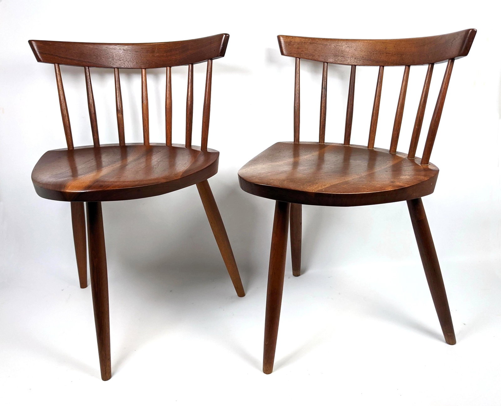 Pr GEORGE NAKASHIMA American Walnut Mira Chairs. Bowed: Pr GEORGE NAKASHIMA American Walnut Mira Chairs. Bowed backrests with spindle construction. Three legged base. Note: This item and all the George Nakashima items from lot 695 though 742 were acquired 