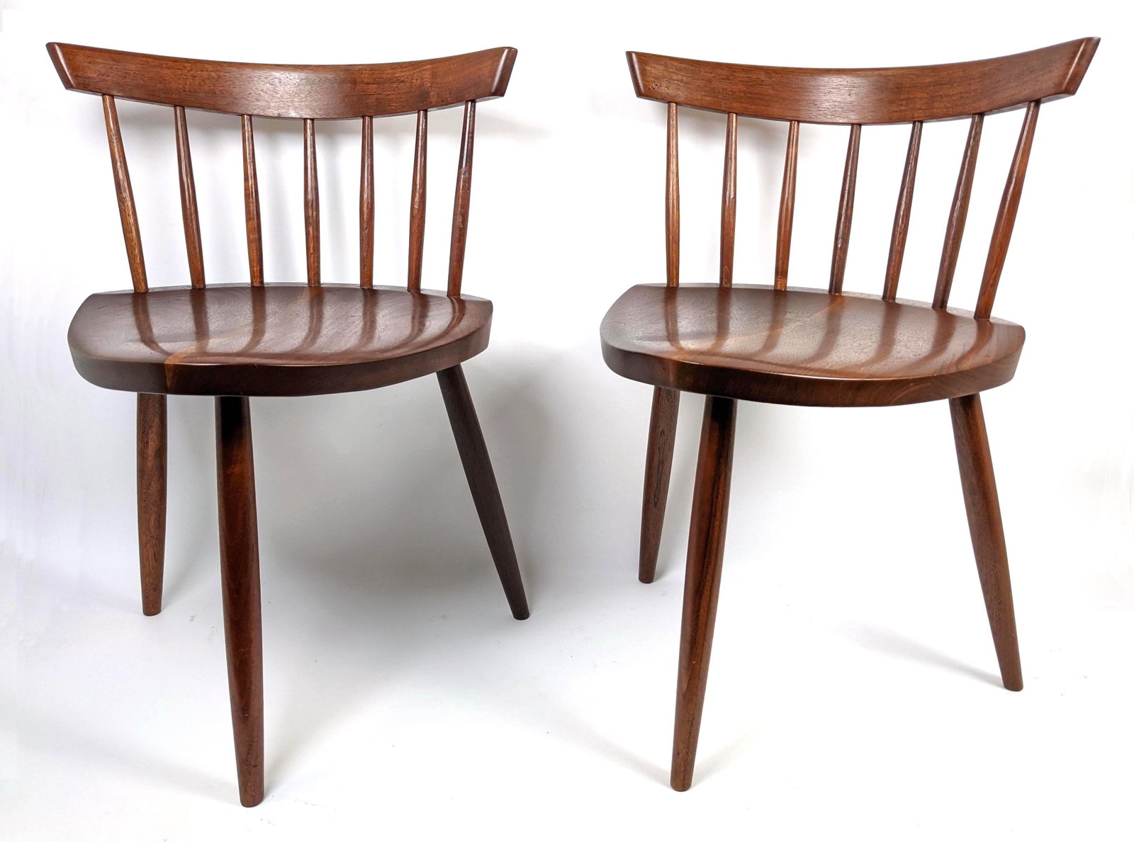 Pr GEORGE NAKASHIMA American Walnut Mira Chairs. Bowed: Pr GEORGE NAKASHIMA American Walnut Mira Chairs. Bowed backrests with spindle construction. Three legged base. Note: This item and all the George Nakashima items from lot 695 though 742 were acquired 