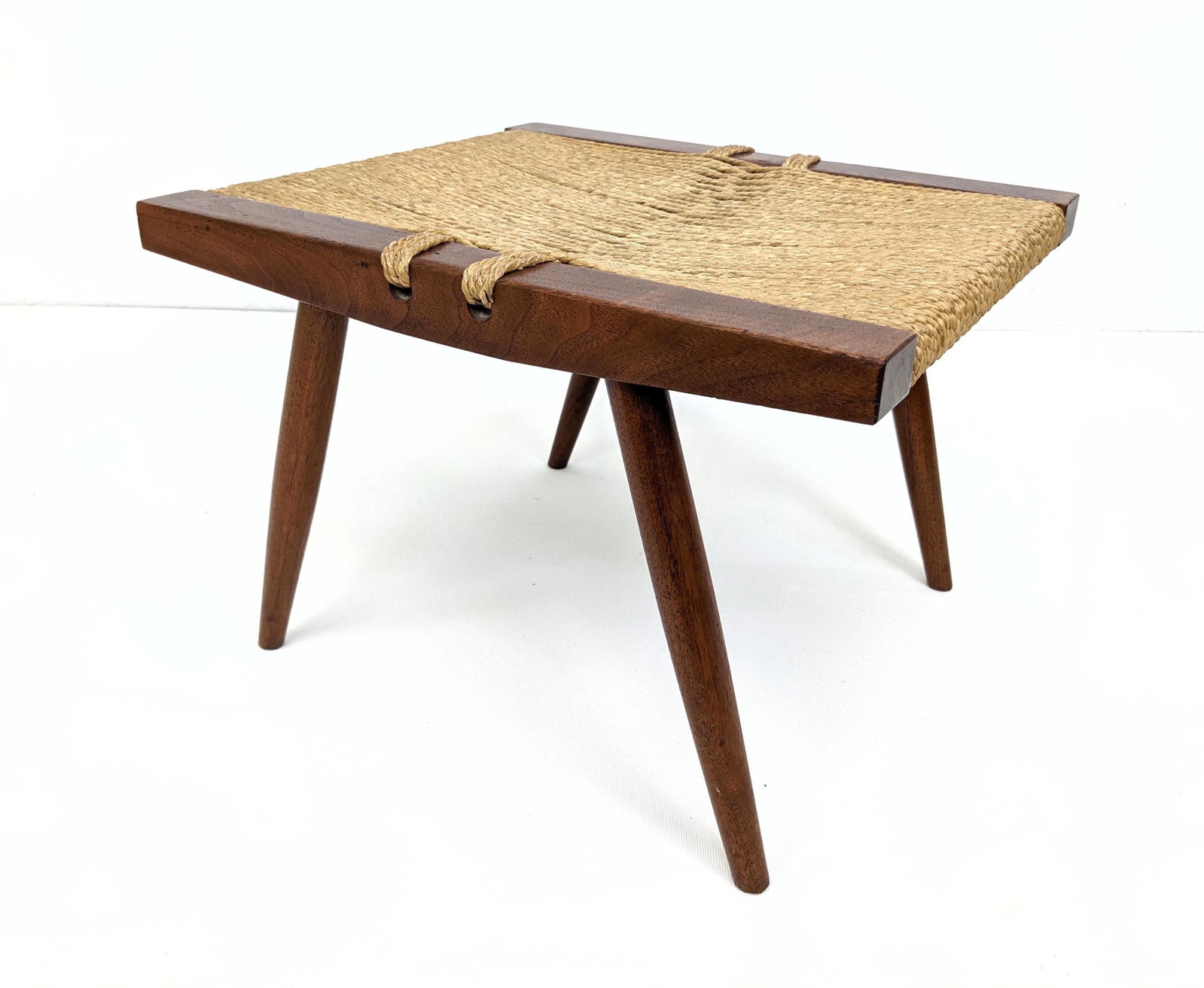 GEORGE NAKASHIMA American Walnut Stool. Woven Sea Grass: GEORGE NAKASHIMA American Walnut Stool. Woven Sea Grass Seated Stool Ottoman. Tapered legs. Note: This item and all the George Nakashima items from lot 695 though 742 were acquired from the estate of 