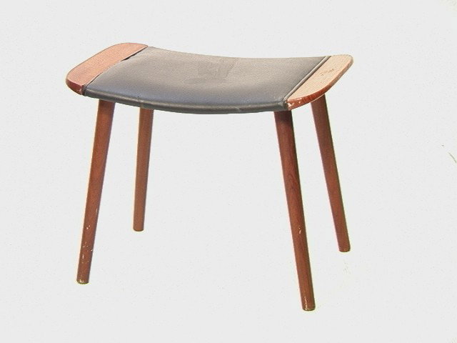 Denmark Teak Upholstered Stool Footrest. Teak Ot: Denmark Teak Upholstered Stool Footrest. Teak Ottoman with tapered peg legs. Black Vinyl. Marked.-- Dimensions: H: 16.5 inches: W: 21 inches: D: 14 inches --- Condition (General): Missing staples at e