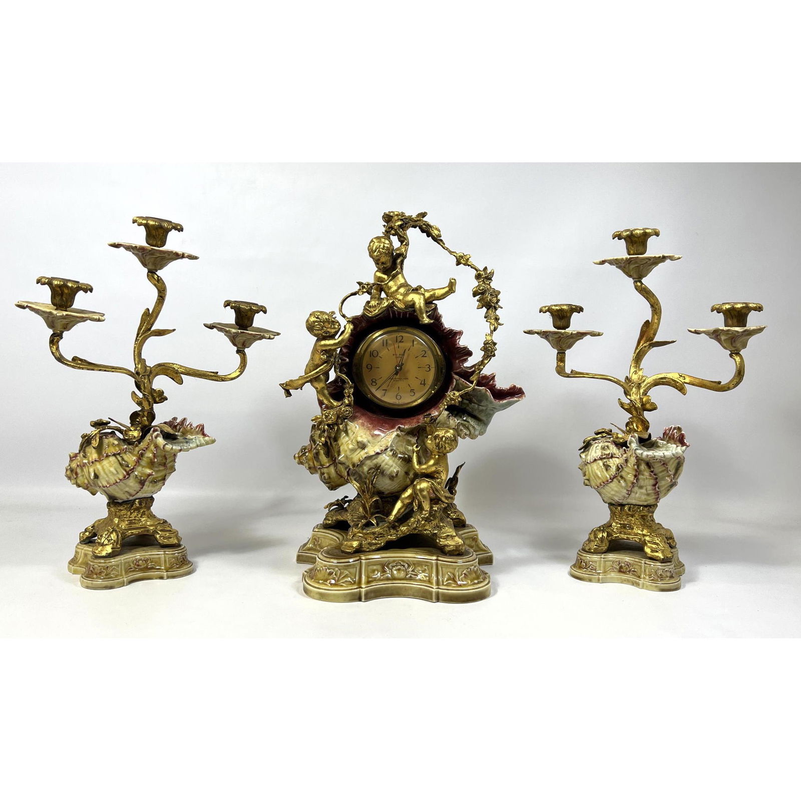 3pc Garniture. Three Arm Candelabra. Majolica Glazed Shells and bases. Center clock has replaced Big: 3pc Garniture. Three Arm Candelabra. Majolica Glazed Shells and bases. Center clock has replaced Big Ben Clock. Dimensions: H: 18.5 inches: W: 12.5 inches: D: 5 inches ---