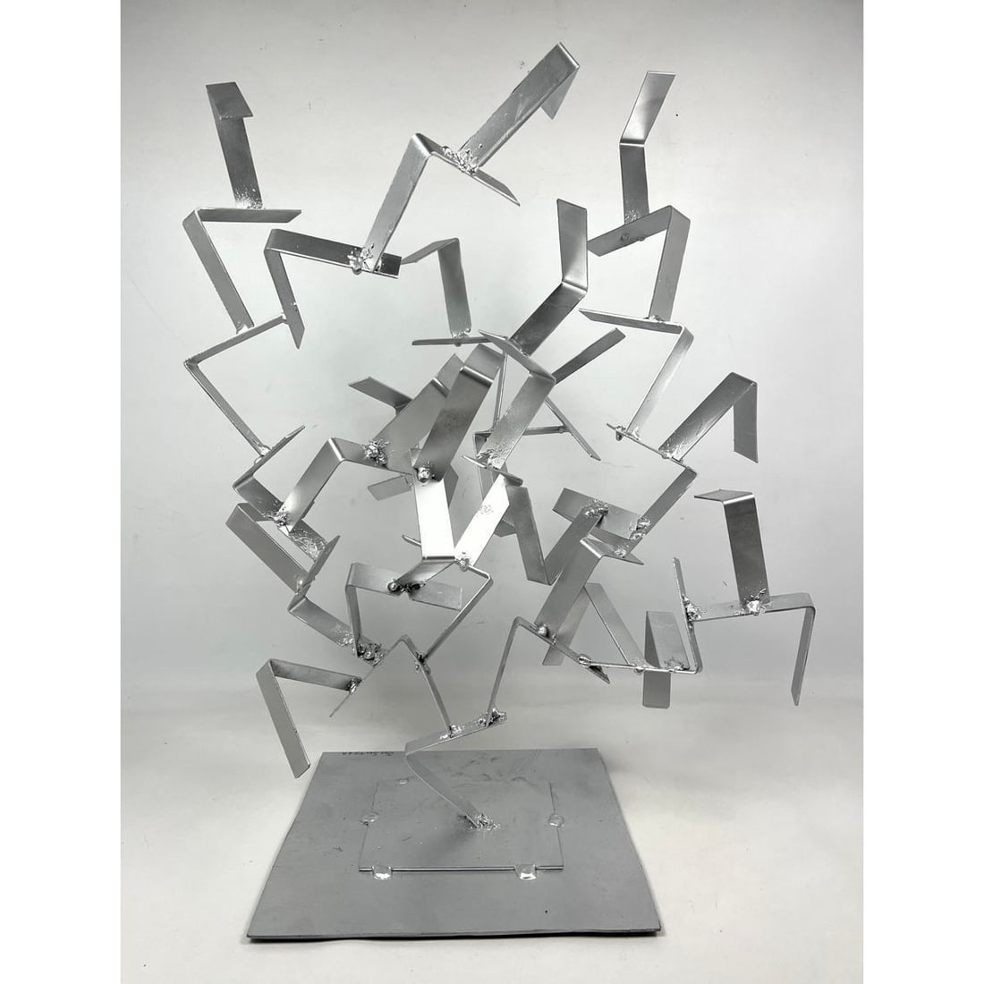 Joe Seltzer, Kinetic Tree Shape Sculpture. Made of found L shaped pieces of steel welded together an: Joe Seltzer, Kinetic Tree Shape Sculpture. Made of found L shaped pieces of steel welded together and to 11" X 12" steel base with felt pads underneath. Signed and painted silver. Dimensions: Height: 