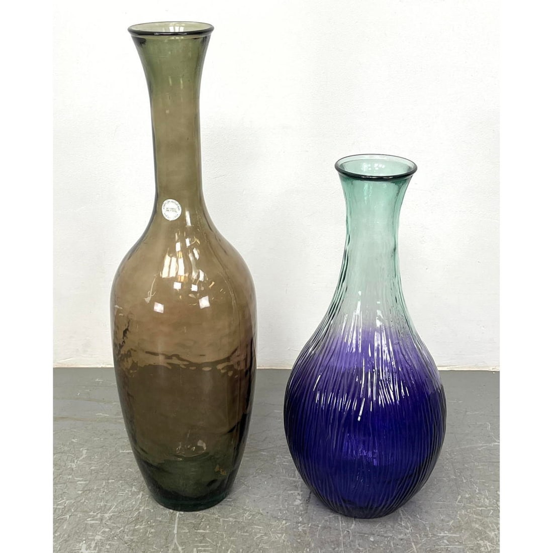 2pc Tall Long Neck Glass Bottle Form Vases. One has paper label: 100% Recycled Glass by VIDRIOS SAN: 2pc Tall Long Neck Glass Bottle Form Vases. One has paper label: 100% Recycled Glass by VIDRIOS SAN MIGUEL, Made in Spain. Dimensions: Height: 39.5 inches, Width: 10.5 inches, Depth: 10.5 inches. - Ad