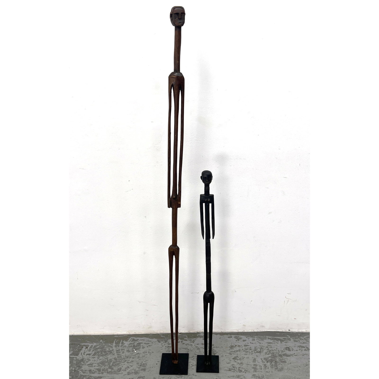 2pcs Tall Narrow African Sculptures. Wood on Steel Plate Base.: 2pcs Tall Narrow African Sculptures. Wood on Steel Plate Base. Dimensions: Height: 60 inches, Width: 5 inches, Depth: 5 inches. - Additional Dimensions: Smaller H: 37 inches, W: 4 inches, D: 4 inches 