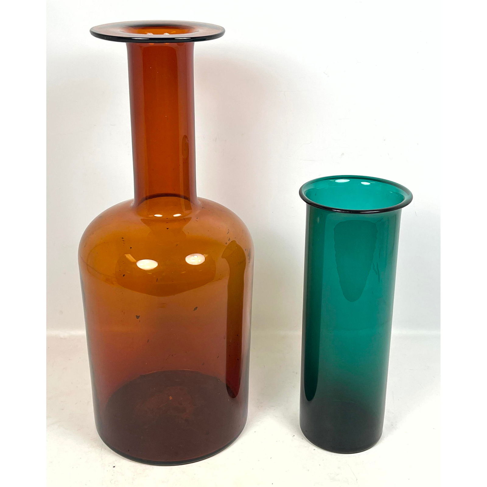 2pc Modernist Glass Vases. Holmegaard style Amber Glass Bottle Form Vase; not marked. Green Cylinder: 2pc Modernist Glass Vases. Holmegaard style Amber Glass Bottle Form Vase; not marked. Green Cylinder Vase. Dimensions: Height: 20 inches, Width: 8.5 inches, Depth: 8.5 inches. --- - We offer curbside