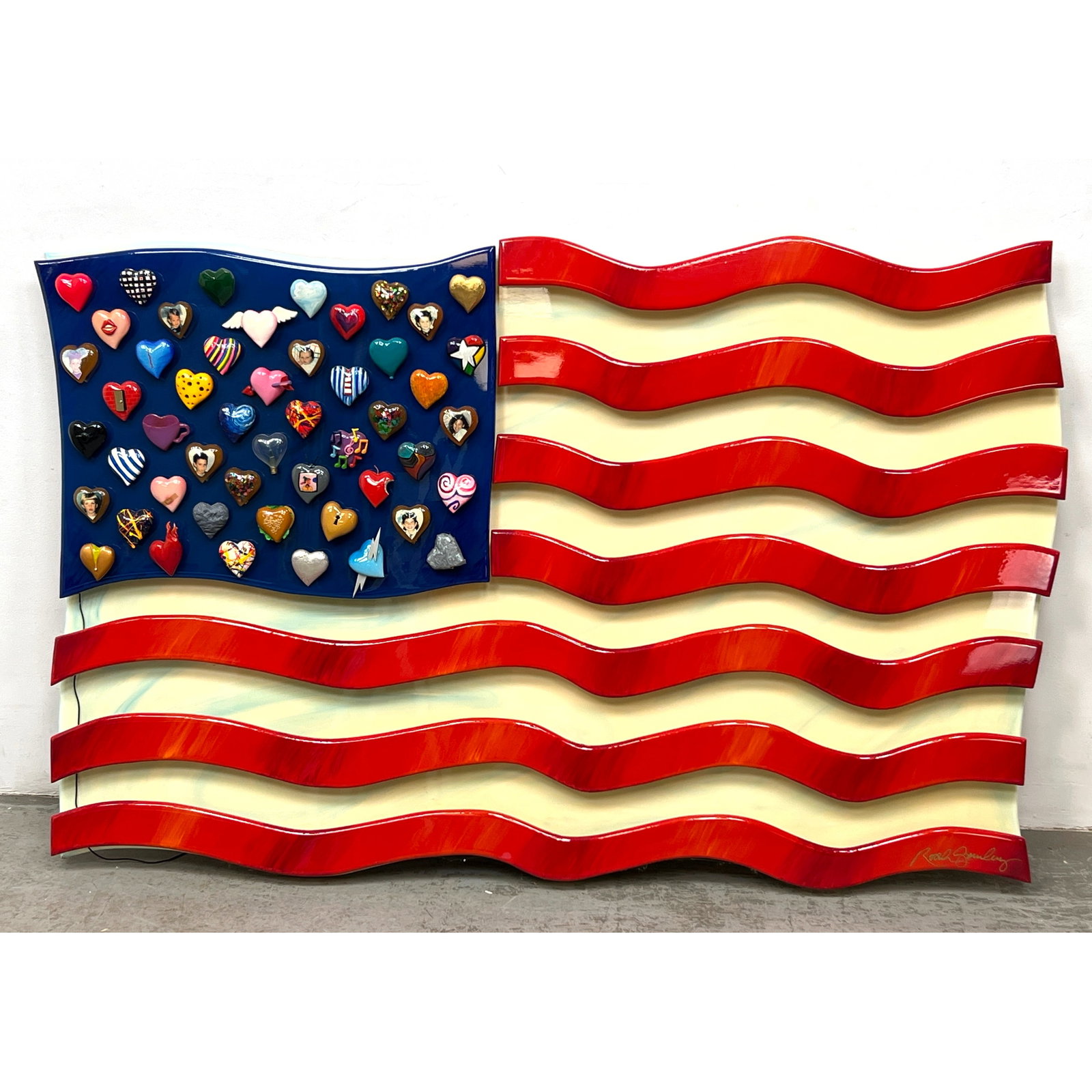 Roark Gourley Large American flag with a high-gloss finish. One heart lights up and blinks. signed R: Roark Gourley Large American flag with a high-gloss finish. One heart lights up and blinks. signed Roark Gourley in gold script on the lower right stripe Dimensions: Height: 45 inches, Width: 70 inche