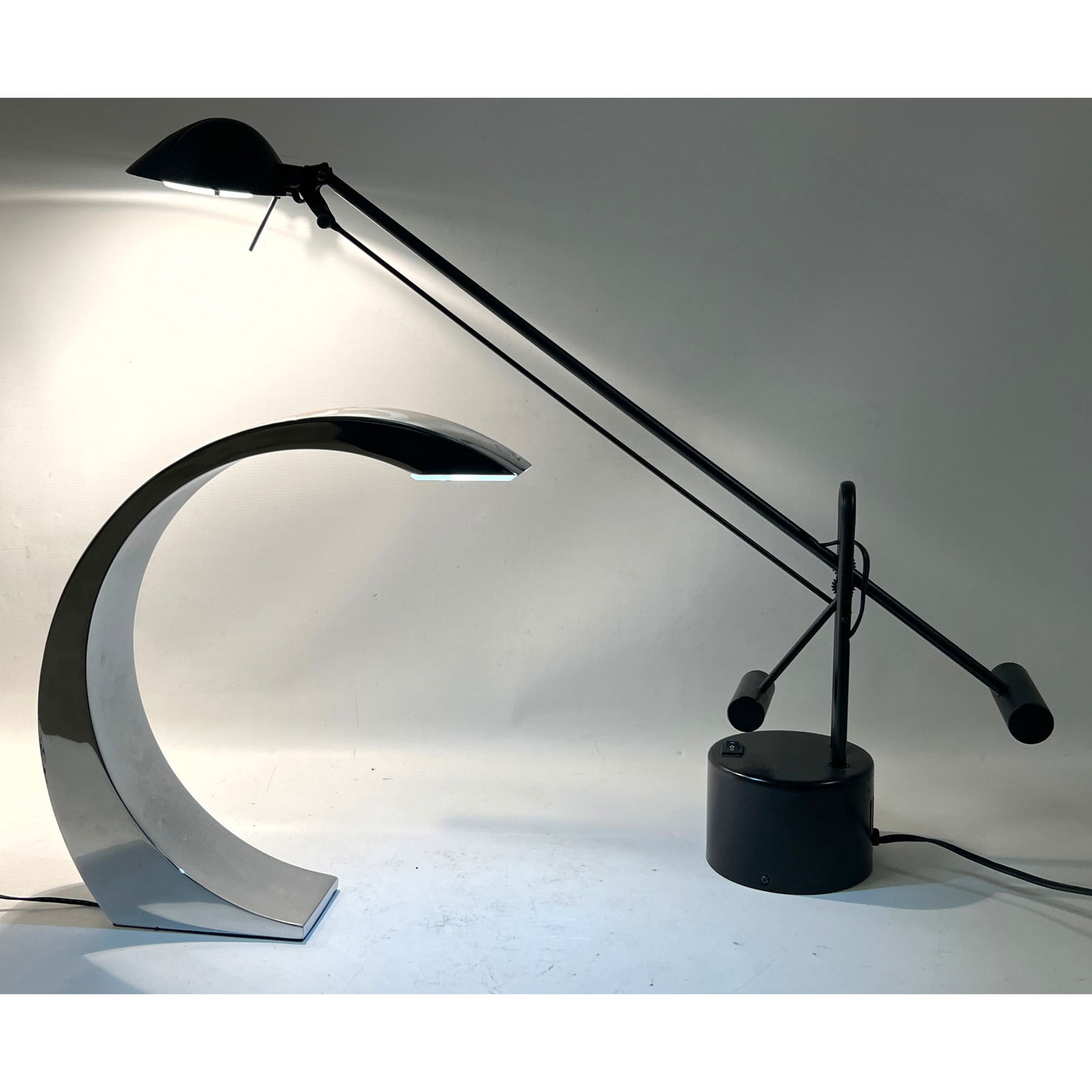 2pc Modernist Lighting. Iconic Table Lamps. Black Cantilever Desk Task Lamp on round base. 2) Chrome: 2pc Modernist Lighting. Iconic Table Lamps. Black Cantilever Desk Task Lamp on round base. 2) Chrome Crescent Curved Accent Lamp. Dimensions: Height: 13.25 inches, Width: 12 inches, Depth: 3 inches. -