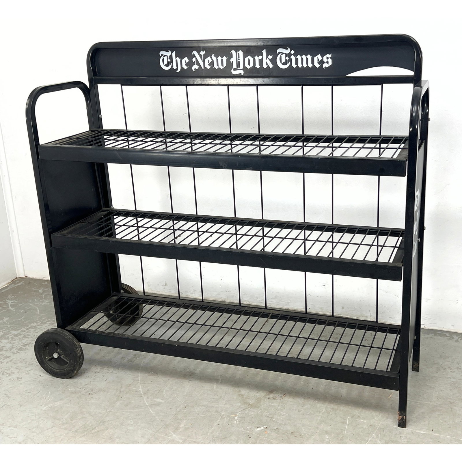 NEW YORK TIMES Vintage Newspaper Cart. Black Metal Rolling Industrial Cart with 3 Wire rod Tiers. NY: NEW YORK TIMES Vintage Newspaper Cart. Black Metal Rolling Industrial Cart with 3 Wire rod Tiers. NYT Logo. Dimensions: Height: 48.5 inches, Width: 52 inches, Depth: 20 inches. ---