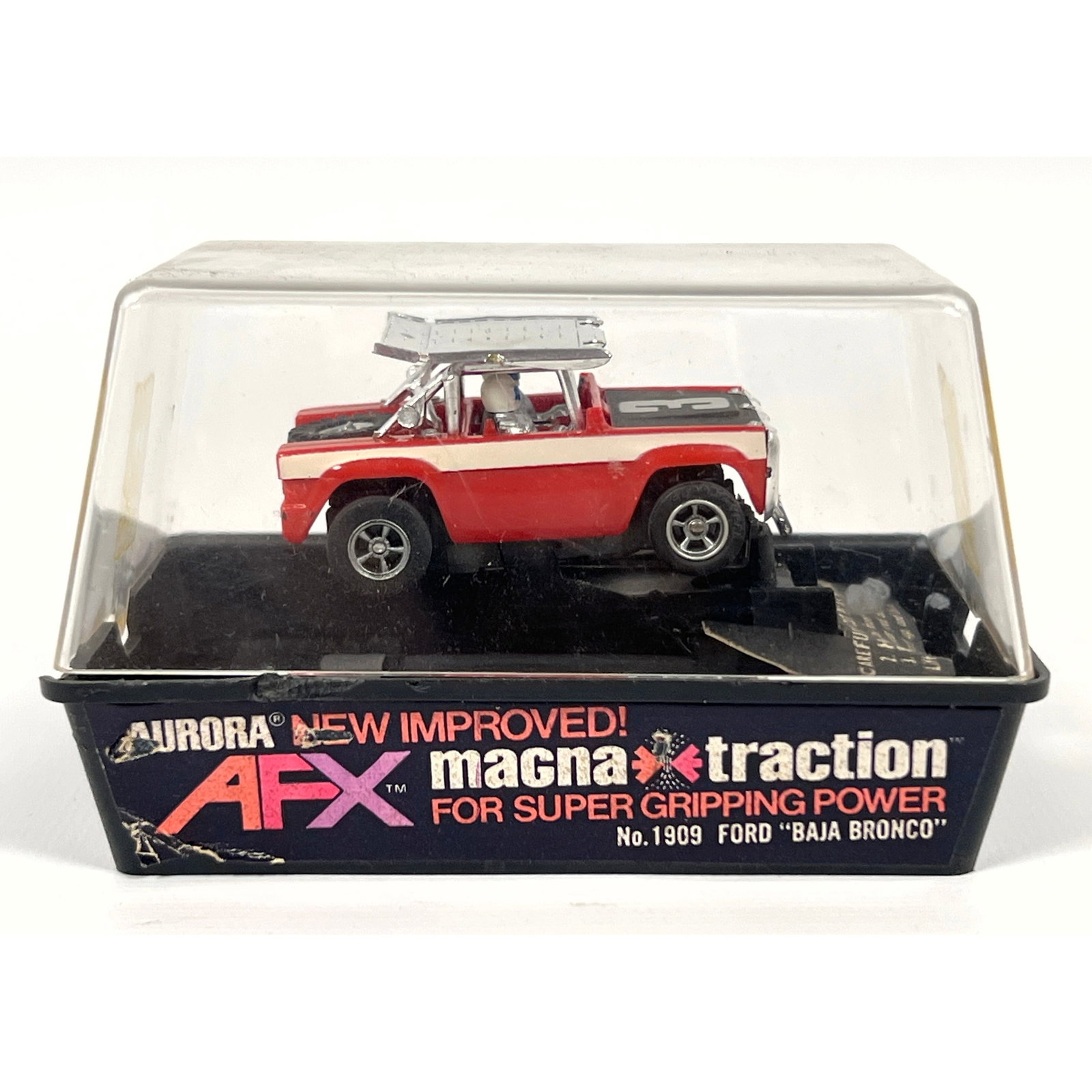Aurora AFX electric slot car is the No. 1909 Ford Baja Bronco model. The vehicle features a plastic: Aurora AFX electric slot car is the No. 1909 Ford Baja Bronco model. The vehicle features a plastic body finished in red and white with a matte black hood displaying a silver number 3. Construction in
