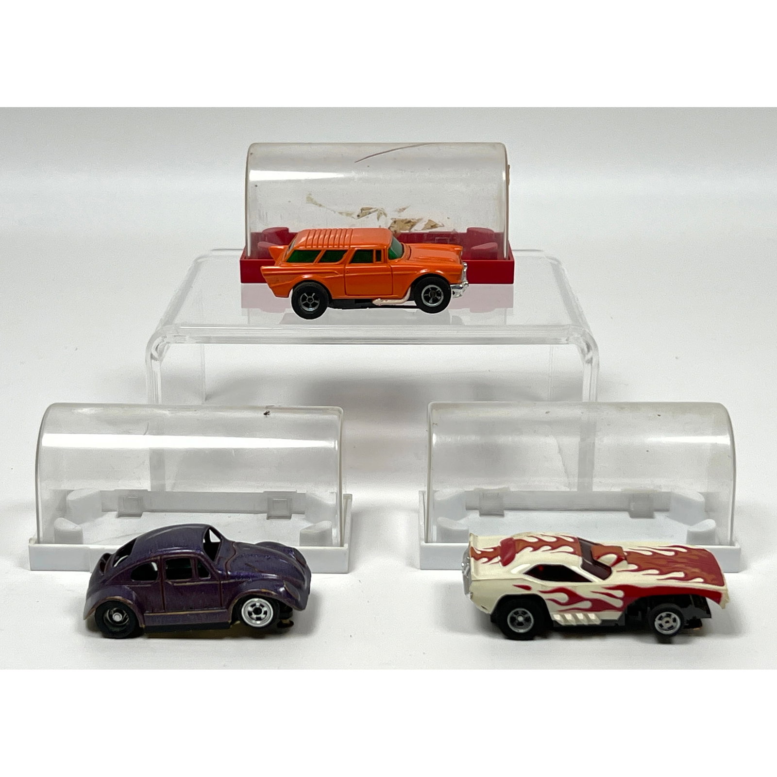 3 HO scale slot cars, each accompanied by an individual plastic display case. The first item is an A: 3 HO scale slot cars, each accompanied by an individual plastic display case. The first item is an Auto World 1957 Chevy Nomad in the Starburst Orange exclusive pattern, featuring a plastic body mount