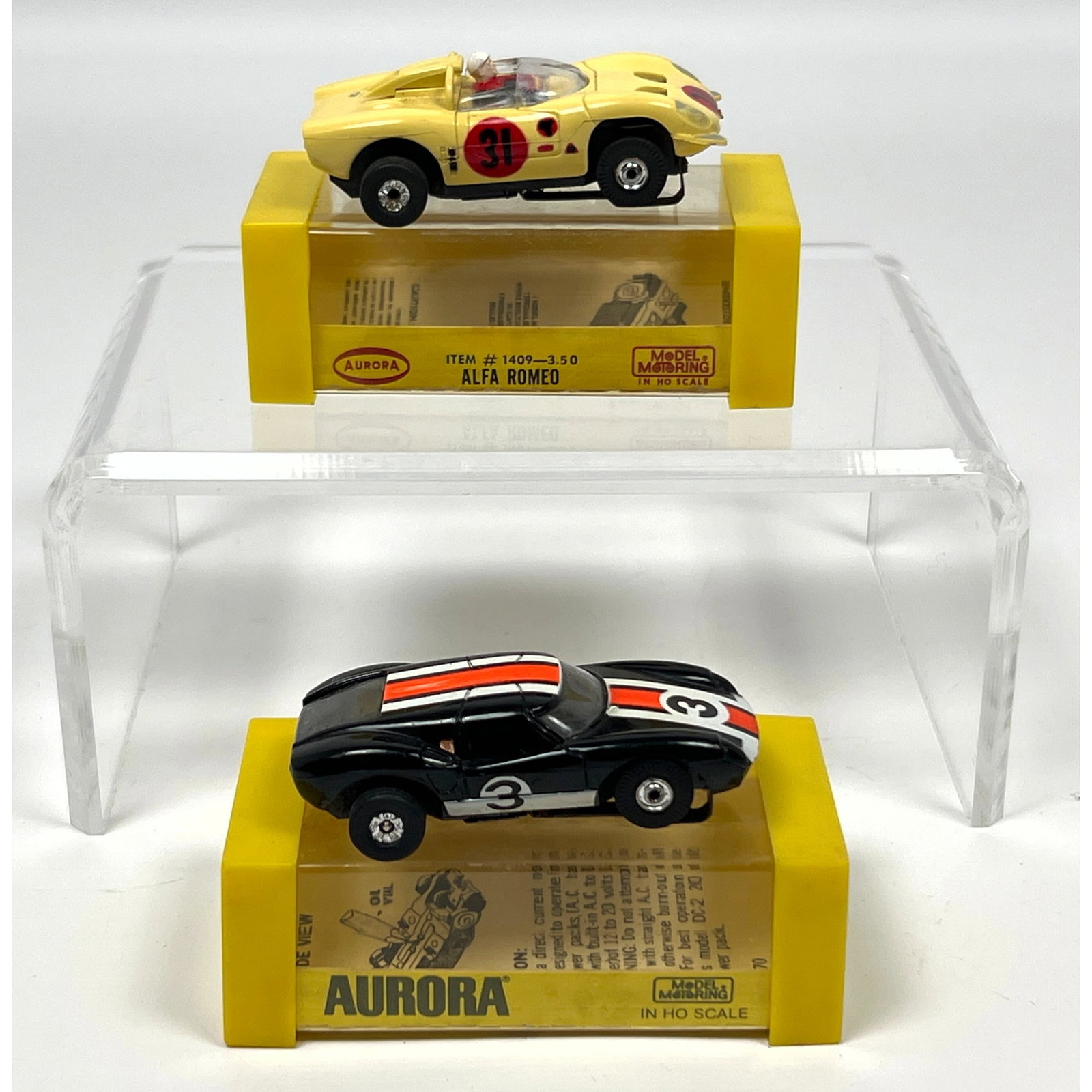 Pair of vintage HO scale electric slot cars manufactured by Aurora as part of the Model Motoring ser: Pair of vintage HO scale electric slot cars manufactured by Aurora as part of the Model Motoring series. The first vehicle is an Alfa Romeo, identified by the packaging as item number 1409. It feature