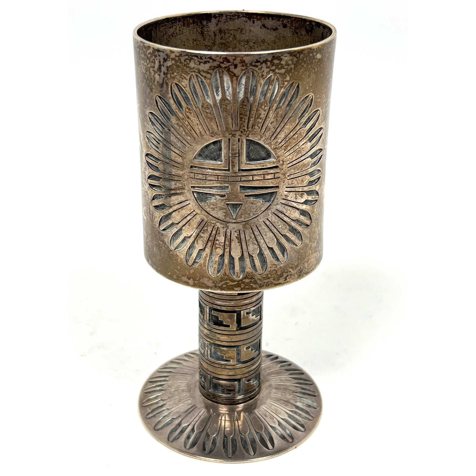 BOBBY TEWA Sterling Silver Navajo Goblet. Central Sunface Motif surrounded by feathers. Round Foot h: BOBBY TEWA Sterling Silver Navajo Goblet. Central Sunface Motif surrounded by feathers. Round Foot has repeating Feather motif. Artist Marked. Dimensions: Height: 5.5 inches, Width: 2.25 inches, Depth