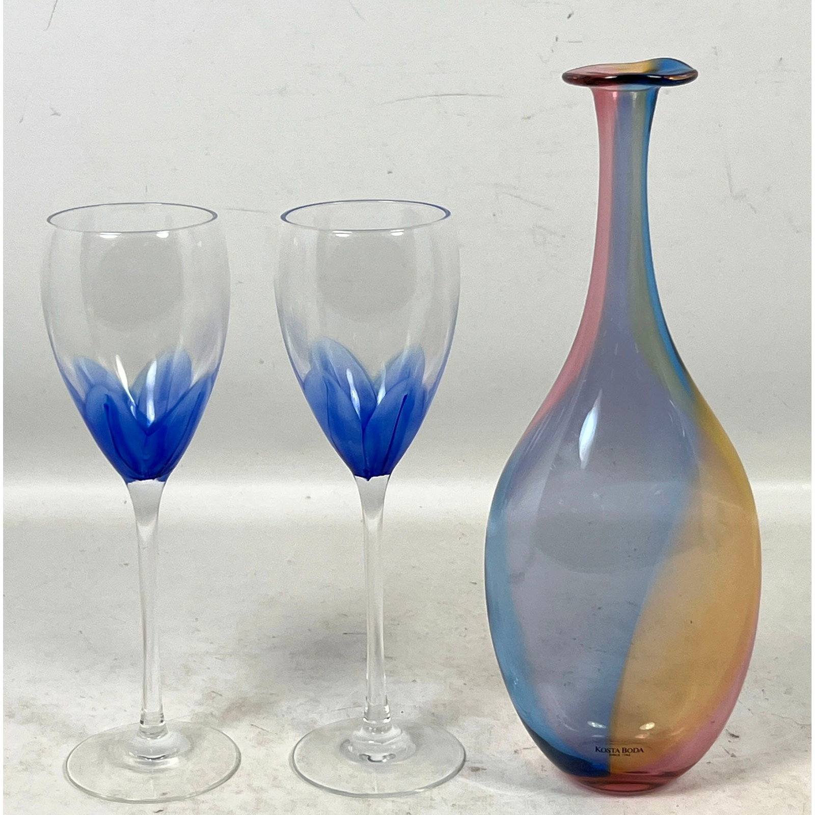 3pc lot of Art Glass featuring Kosta Boda Kjell Engman Decanter and a Pair of Craig Mardock Signed B: 3pc lot of Art Glass featuring Kosta Boda Kjell Engman Decanter and a Pair of Craig Mardock Signed Blue Tulip Wine Glasses Dimensions: Height: 11 inches, Width: 4 inches, Depth: 2 inches. --- US Packi
