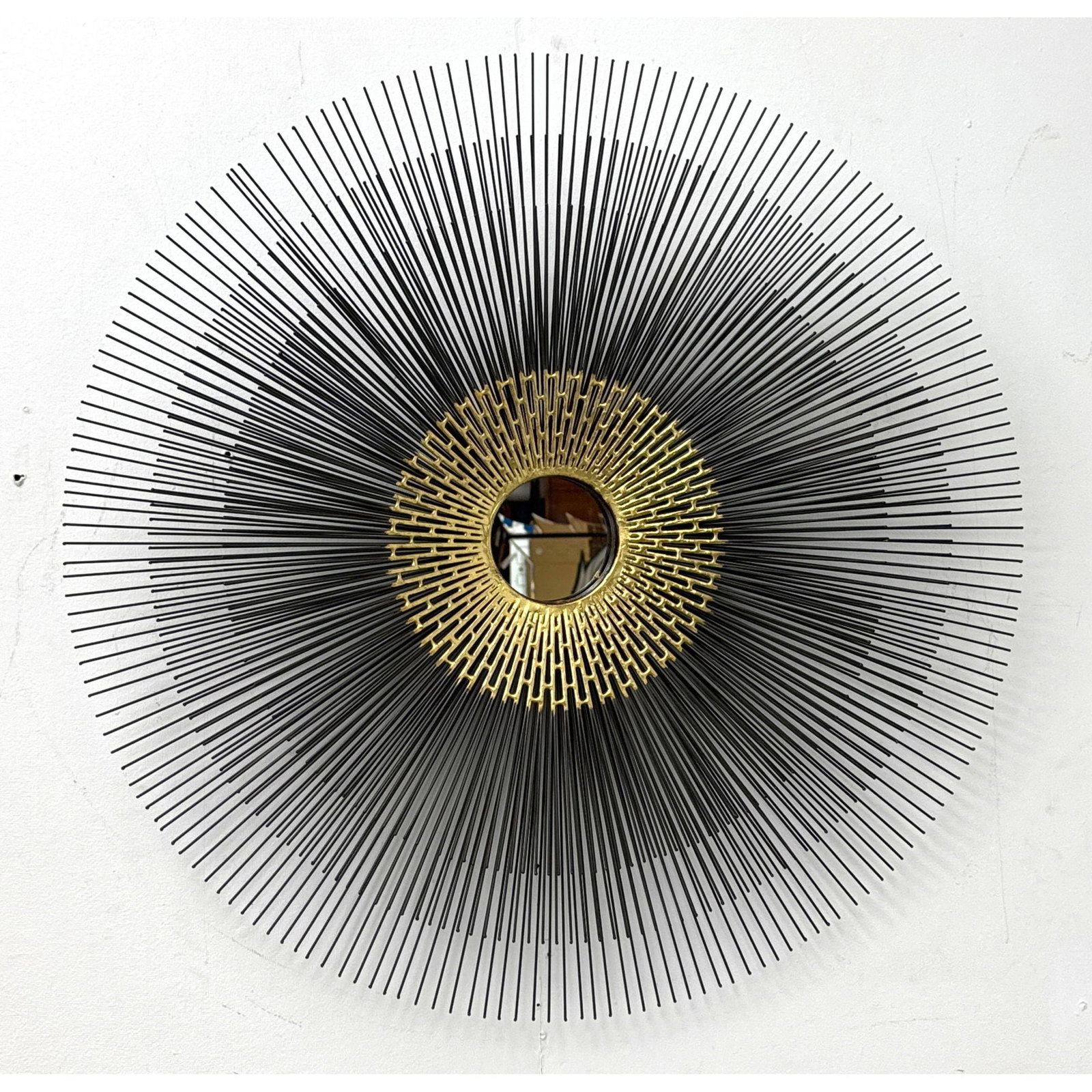 Large Brutalist sunburst wall mirror in the style of William Friedle with 2 tiered black wire spokes: Large Brutalist sunburst wall mirror in the style of William Friedle with 2 tiered black wire spokes and textured gold toned center Dimensions: Height: 30 inches, Width: 30 inches. ---