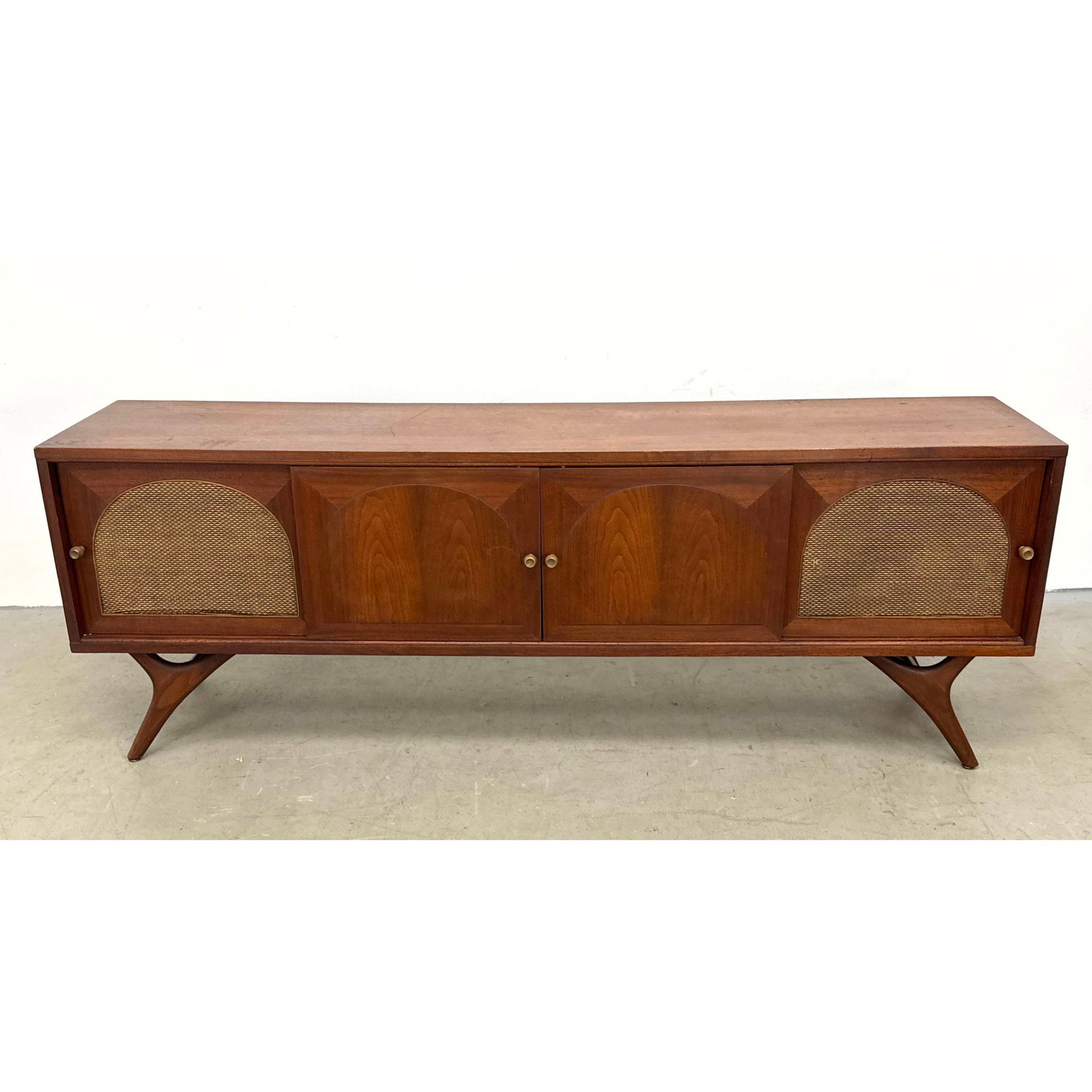 Mid-Century Modern walnut console credenza featuring sliding doors with recessed arch and woven gril: Mid-Century Modern walnut console credenza featuring sliding doors with recessed arch and woven grille panels Dimensions: Height: 25.5 inches, Width: 71 inches, Depth: 15.5 inches. ---