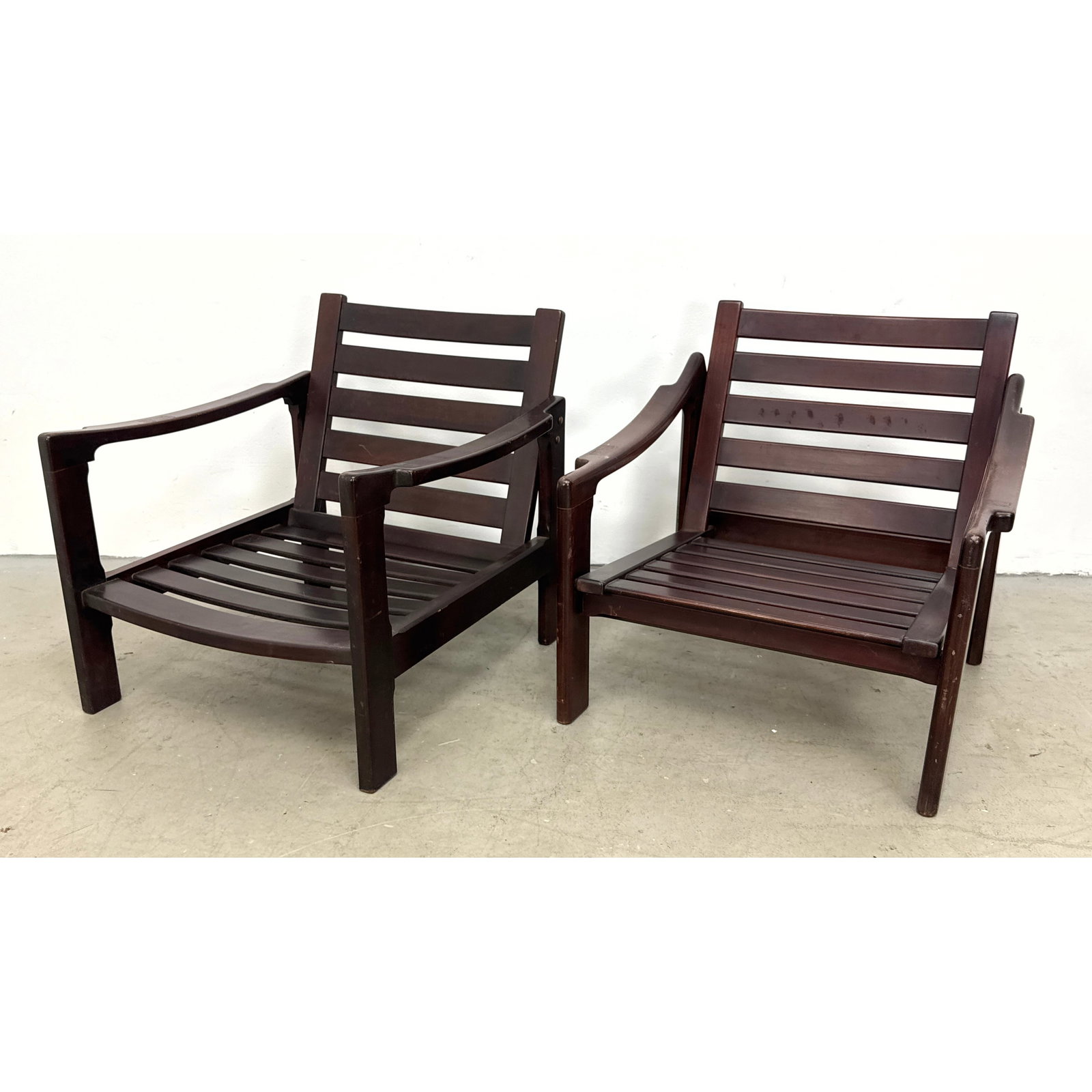 Pair mid century modern slatted wood lounge armchairs with sculpted sweeping armrests and dark finis: Pair mid century modern slatted wood lounge armchairs with sculpted sweeping armrests and dark finish. Unsigned. Dimensions: Height: 24.25 inches, Width: 25.75 inches, Depth: 26 inches. - Seat Height: