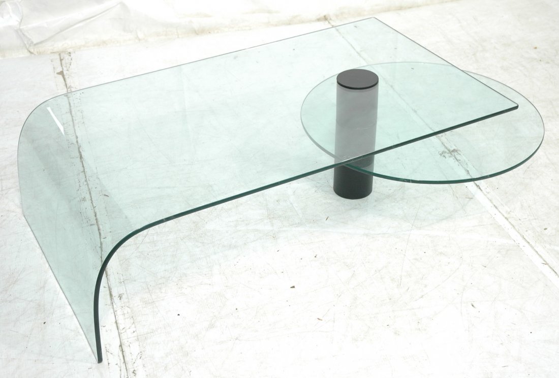 Italian Glass Two Tier Coffee Table. Sloped upper: Italian Glass Two Tier Coffee Table. Sloped upper level. Round lower glass shelf can swing out. Black metal column frame. 1/2" thick glass.-- Dimensions: H: 16 inches: W: 50.5 inches: D: 30.5 inches -