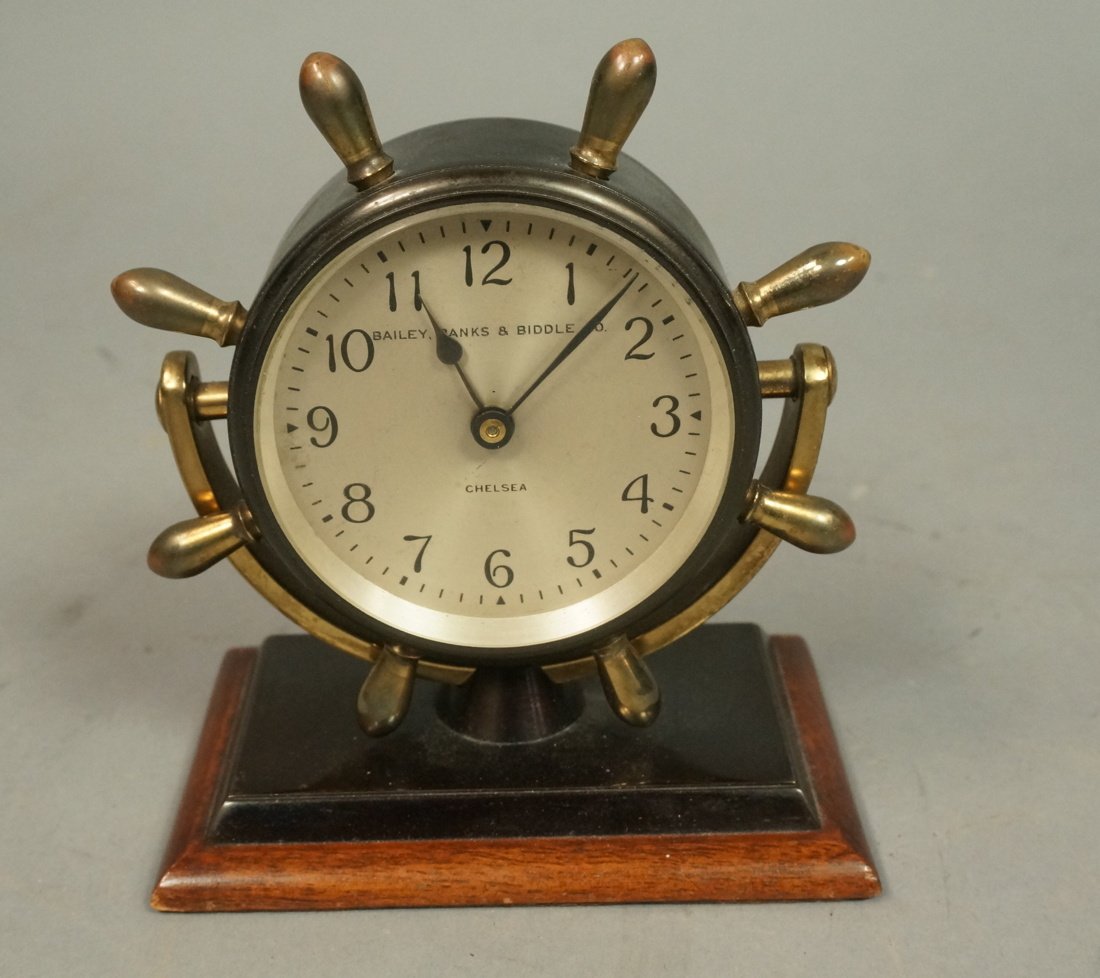 CHELSEA Ships Wheel Desk Clock. BAILEY BANKS & BI: CHELSEA Ships Wheel Desk Clock. BAILEY BANKS & BIDDLE. Black metal with brass details. Mounted on wood base. Marked-- Dimensions: H: 5 inches: W: 4.5 inches: D: 3 inches --- US Shipping charge: $35