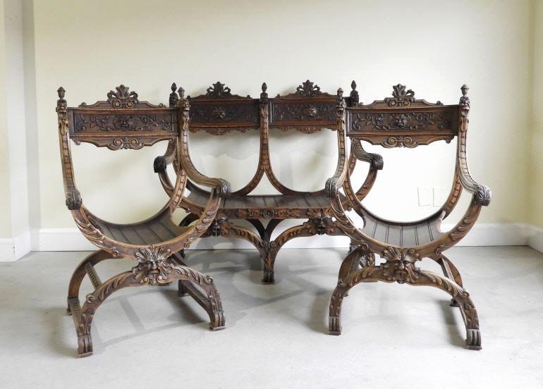 ITALIAN RENAISSANCE REVIVAL OAK ARMCHAIRS & SETTEE: A late 19th century suite of two Italian Renaissance Revival Savonarola oak arm chairs and matching settee, all with chip carved decoration, outstretched armrests terminating to lions head grips and "