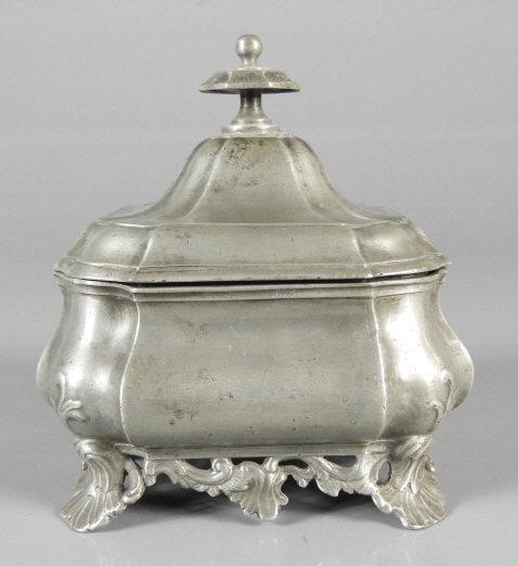 GOOD PEWTER ROCOCO PERIOD SUGAR BOX: A good pewter Rococo period lidded sugar box. A shaped and knopped lid over an ogee body resting on a foliate inspired base. Continental quality mark of an angel holding scales, used to signify good q