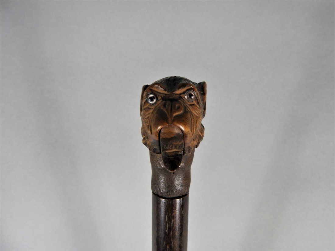 NOVELTY GLOVE HOLDING WALKING STICK: A novelty walking - swagger stick, the carved pommel fashioned as a monkey set with glass eyes. The spring loaded mouth opens to serve as a glove clip. Length, 35".