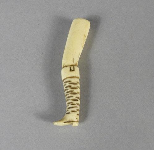 GEORGIAN BONE PIPE TAMPER, CIRCA 1820: A Georgian period carved bone pipe tamper, modeled as a man's leg, the buttoned trouser fitted into a high top leather boot. Circa 1820. Length, 3”.