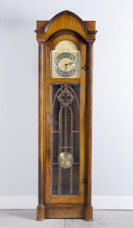 WALNUT TALL CASE CLOCK, EARLY 20TH CENTURY: A Gothic inspired walnut tall case clock. Fretwork on the door. Sided columns rise to an arched top. The clock face well decorated. Early 20th Century.