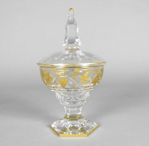 VAL SAINT LAMBERT CRYSTAL LIDDED JAR: A 20th century Val Saint Lambert crystal lidded jar, showing a faceted cut body decorated with gilded motifs of grapes and vinery, rising from a short hexagonal stem atop a conforming foot. Height, 10