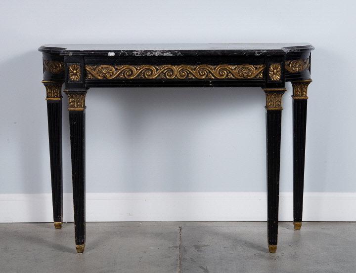 EMPIRE STYLE EBONIZED CONSOLE TABLE: A late 20th century ebonized and parcel gilt Empire style console table, showing a curvilinear black and white marble top over a conforming frieze decorated with vitruvian scrolls and shell motifs, ra