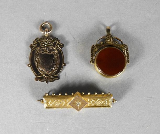 VICTORIAN GOLD JEWELLERY: Three pieces of Victorian .375 (9kt) yellow gold jewellery. (1) A swiveling watch fob with carnelian and bloodstone. (2) An heraldic looking pendant marked for Birmingham. (3) A rectangular brooch mar