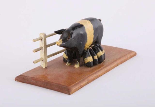 Carving, Sow & Piglets, by Bruce Smith, C. 1970: A folk art carving by Bruce Smith of Bethany Ontario of a Wessex Saddleback sow (black with white stripe) and eight suckling piglets on a wood base with white fence behind. Circa 1970. H: 4"; W: 9"; D
