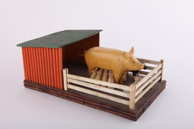 Carving, Sow & Piglets, by Bruce Smith: A folk art carving of a standing sow in a fenced lean-to with eight suckling piglets, all in original paint. Attributed to Bruce Smith, Bethany, Ontario. Circa 1970. H: 5"; W: 12"; D: 7".