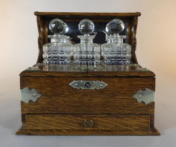 English Oak Case Tantalus, Early 20th Century: An early 20th century English oak cased 3 bottle tantalus with applied silver plated mounts and carrying handles, fitted with 3 stoppered cut glass decanters fronted by two hinged panels opening to a 