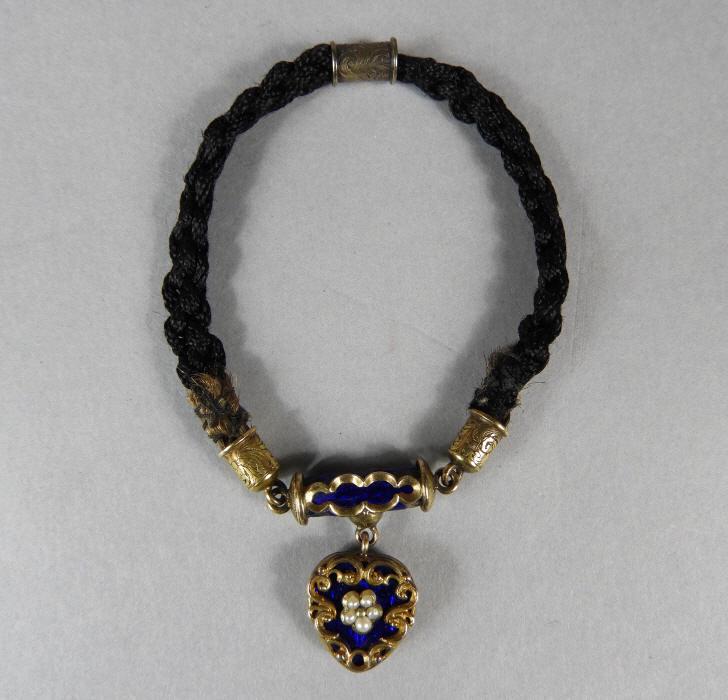 Heart Shaped 14KT Gold Mourning Bracelet: A very good mid 19th century 14KT gold mourning bracelet, the black braided band coupled to a cobalt enamelled bar holding a heart-shaped locket with cobalt enamel, seed pearls and gilt scrollwork, th