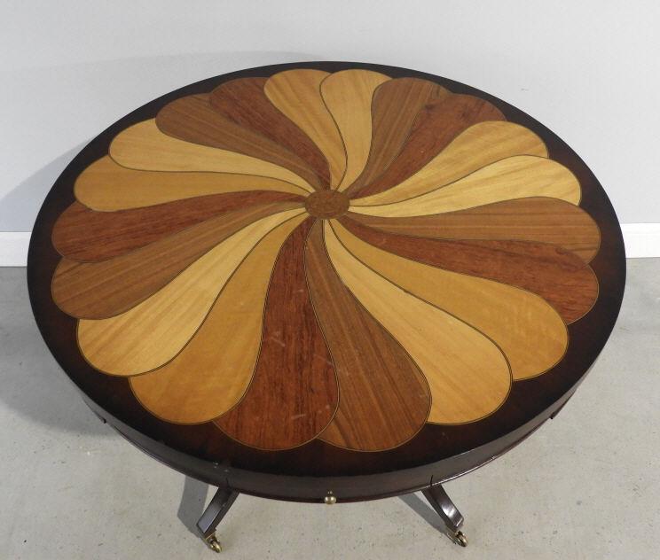 Contemporary Drum Table: A 'specimen' drum table, the circular top panelled with various exotic woods fanning out above a conforming frieze fitted with 4 small drawers, raised on 4 in-swept supports on brass casters. Minor we